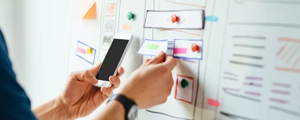Person hält Smartphone vor Whiteboard mit Notizen