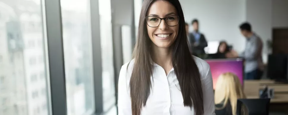 Person mit Brille lächelt in einem modernen Büro.