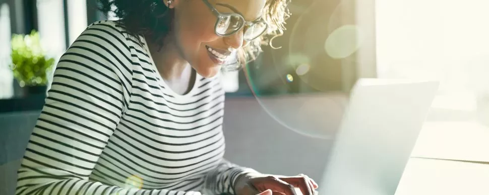 Person mit Brille arbeitet am Laptop in einem sonnigen Raum.
