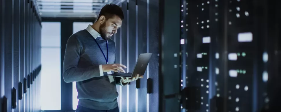 Person mit Laptop in einem Serverraum.