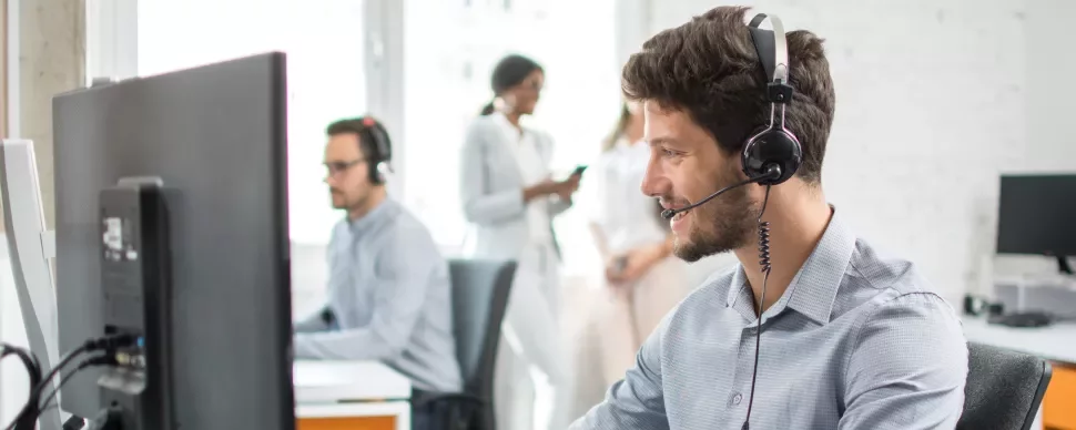 Person im Büro trägt ein Headset und arbeitet am Computer.