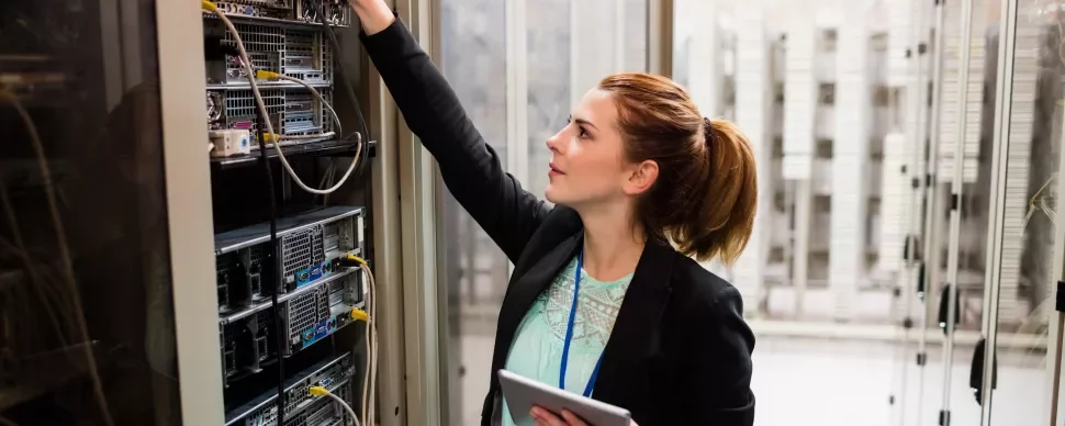 Person in einem Serverraum überprüft die Hardware mit einem Tablet in der Hand.