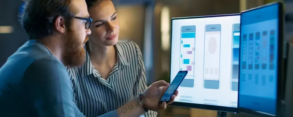 Zwei Personen betrachten Smartphone-Designs auf Bildschirmen.