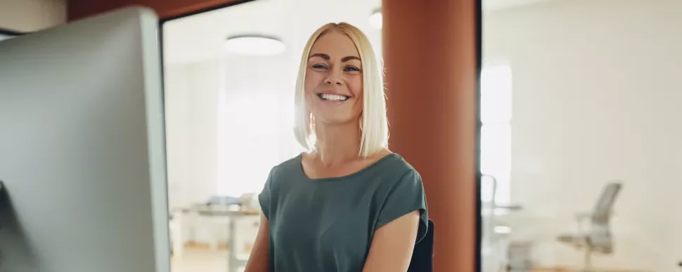Person lächelt am Schreibtisch in einem modernen Büro.