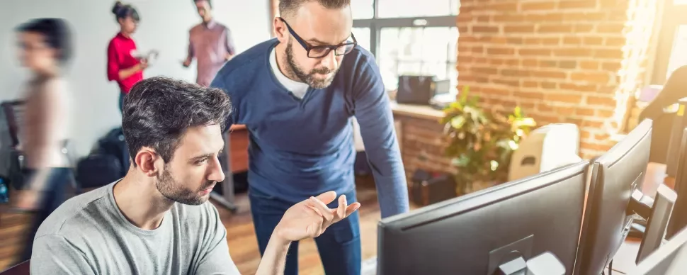 Zwei Personen arbeiten gemeinsam an einem Computerbildschirm im Büro.