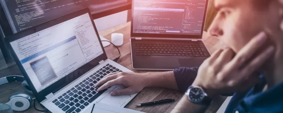 Person arbeitet an Laptop mit Code auf Bildschirm.