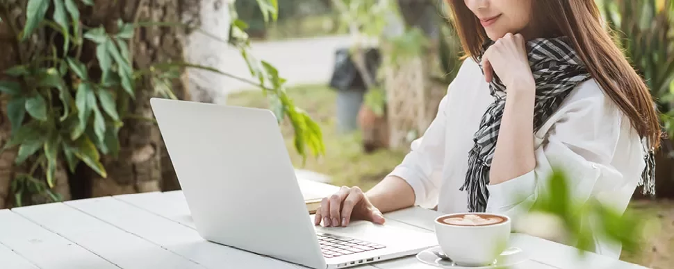 Person arbeitet am Laptop im Freien neben einer Tasse Kaffee.