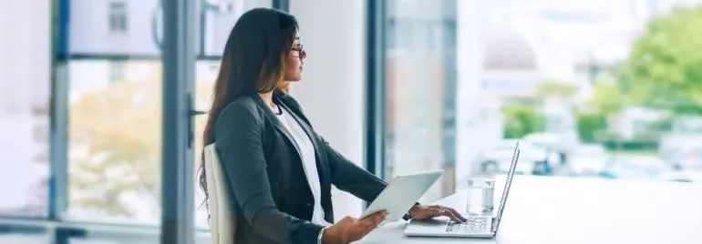 Person arbeitet am Laptop und Tablet in einem Büro
