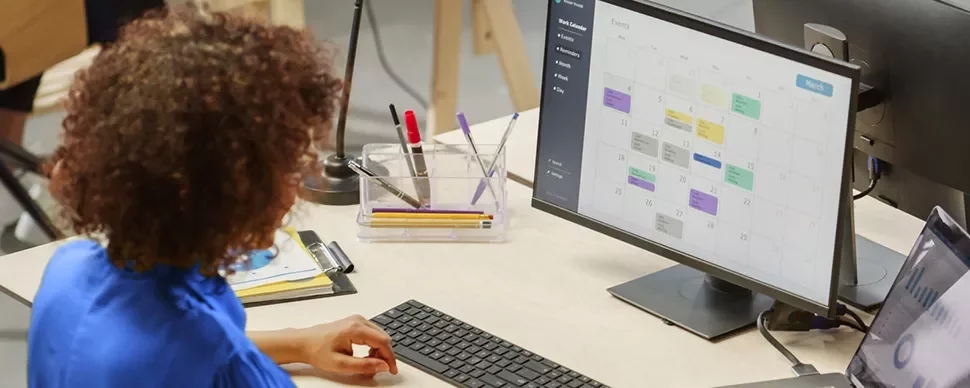 Person arbeitet am Schreibtisch mit Kalender auf Bildschirm