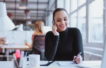 Person telefoniert in modernem Büro und macht Notizen.