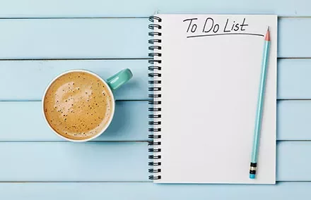 Notizbuch mit der Aufschrift 'To Do List' und einem Bleistift neben einer Tasse Kaffee auf blauem Tisch.