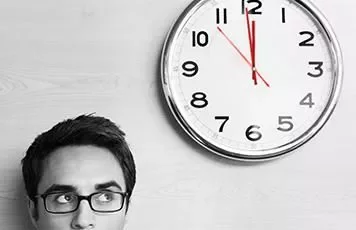 Person mit Brille schaut auf eine große Wanduhr.