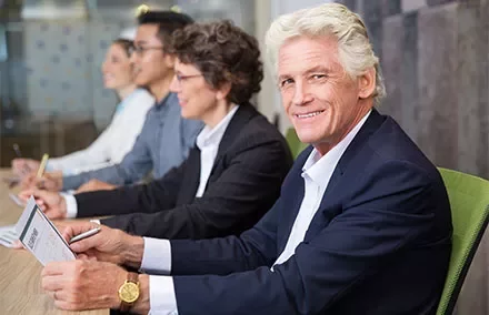 Personen bei einem Meeting, lächelnd und Notizen machend.