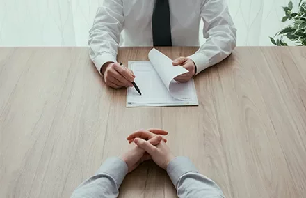 Zwei Personen an einem Tisch im Gespräch, eine zeigt auf ein Dokument.