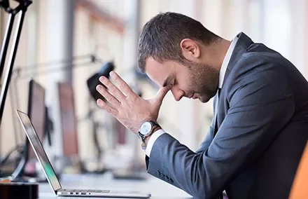 Person stützt den Kopf auf die Hände vor einem Laptop im Büro.