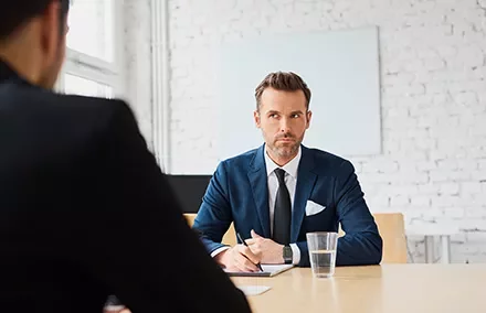 Person in Anzug sitzt an einem Tisch bei einem Meeting.