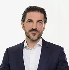 Person in Anzug mit weißem Hemd vor neutralem Hintergrund.
