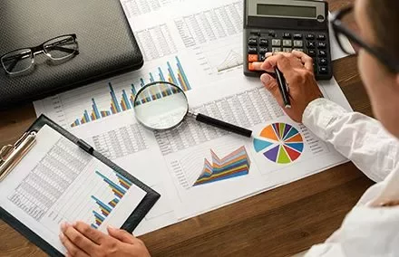 Person analysiert Diagramme und Berechnungen mit Taschenrechner.
