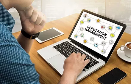 Person arbeitet an einem Laptop mit der Aufschrift 'Reputation Management'.
