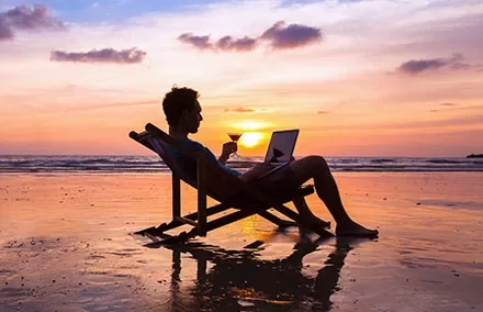 Person entspannt am Strand mit Laptop bei Sonnenuntergang.