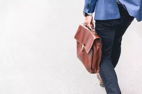 Person mit blauer Jacke trägt eine braune Ledertasche.