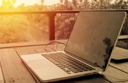 Laptop auf einem Holztisch bei Sonnenuntergang.